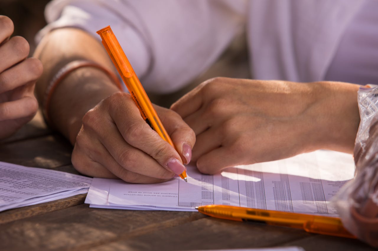 our-story Close-up shot of hands writing on documents with orange pen, implying business or education setting.