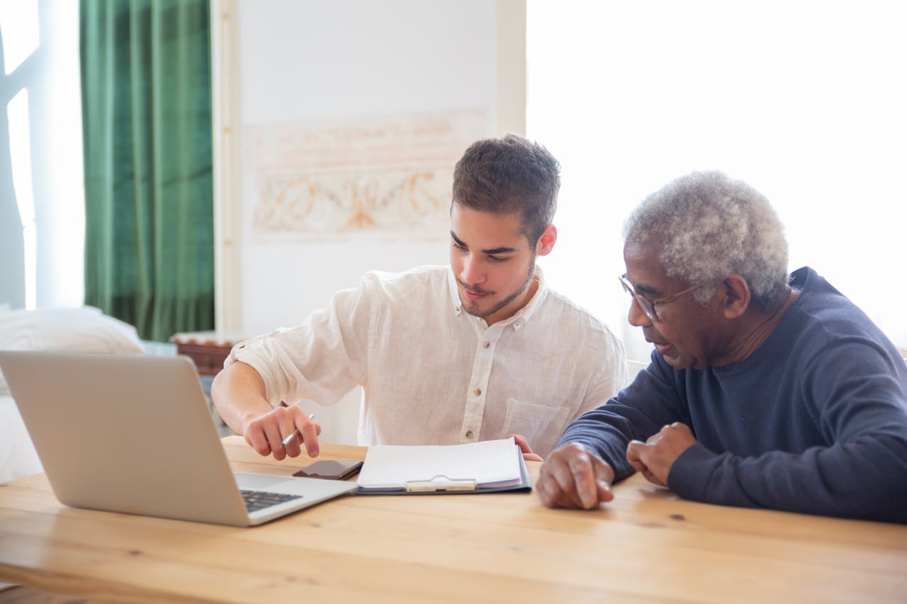 about-us Young man teaches elderly gentleman to use technology at home.